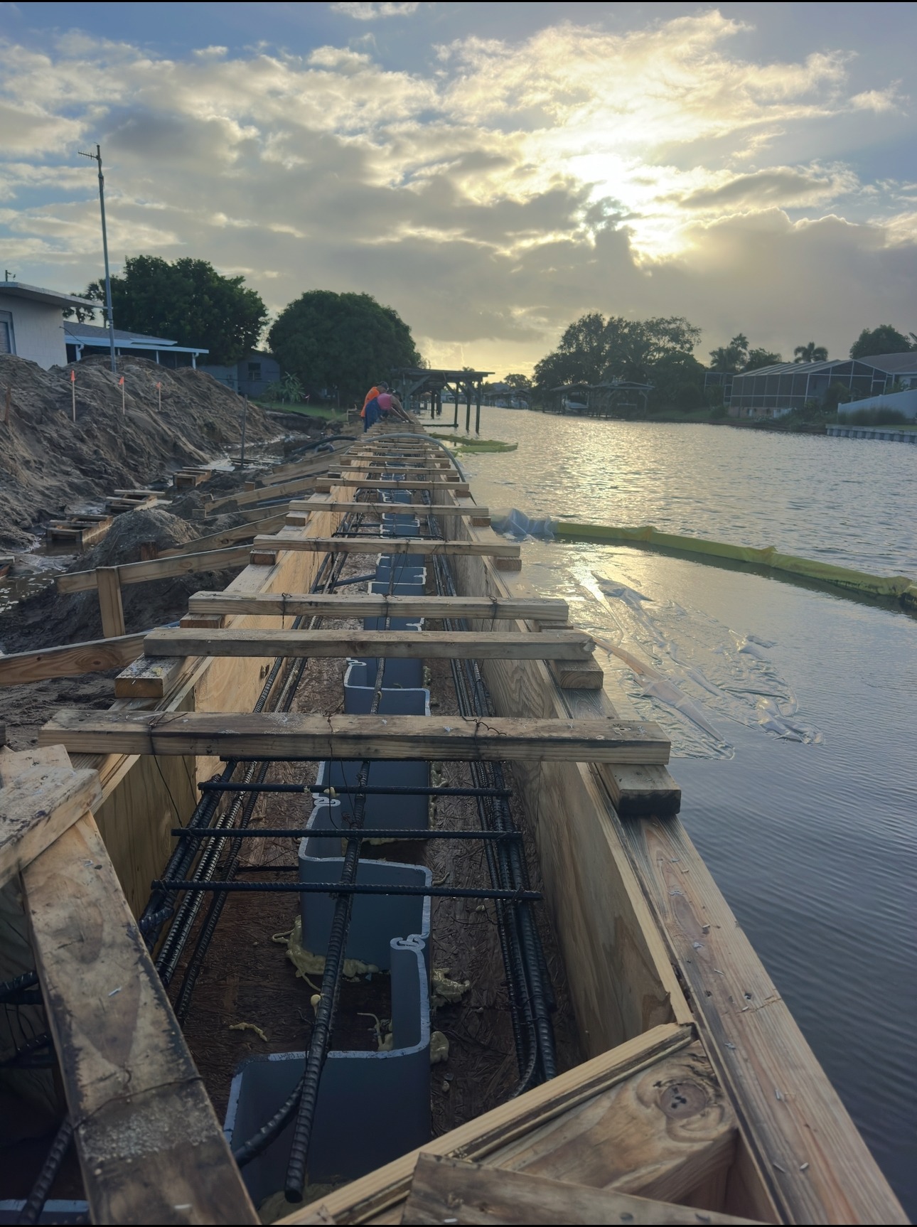 Site logistics and formwork staged along the waterfront at sunset